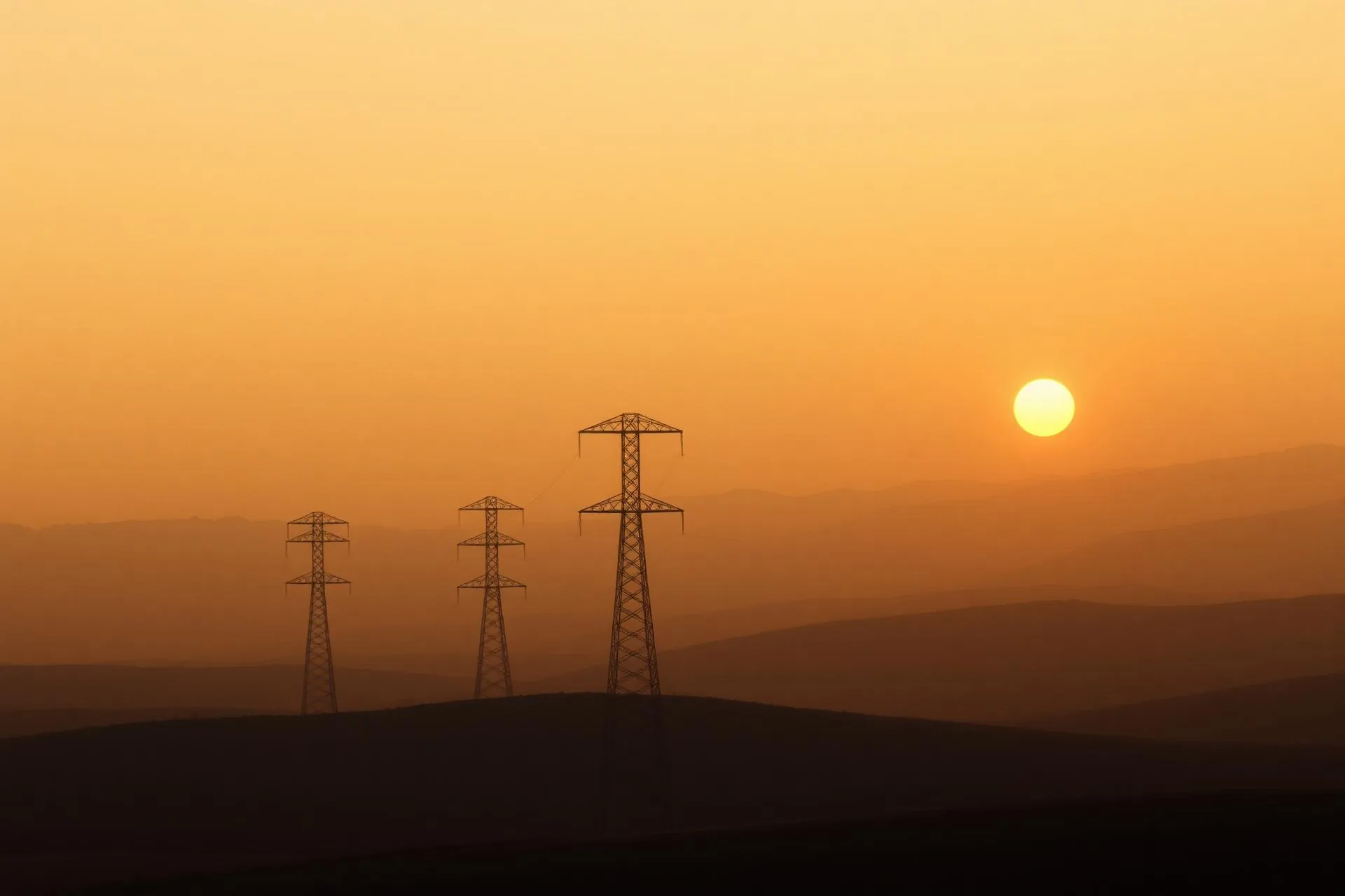 Lattice transmission towers marching across a warm desert plain at dusk